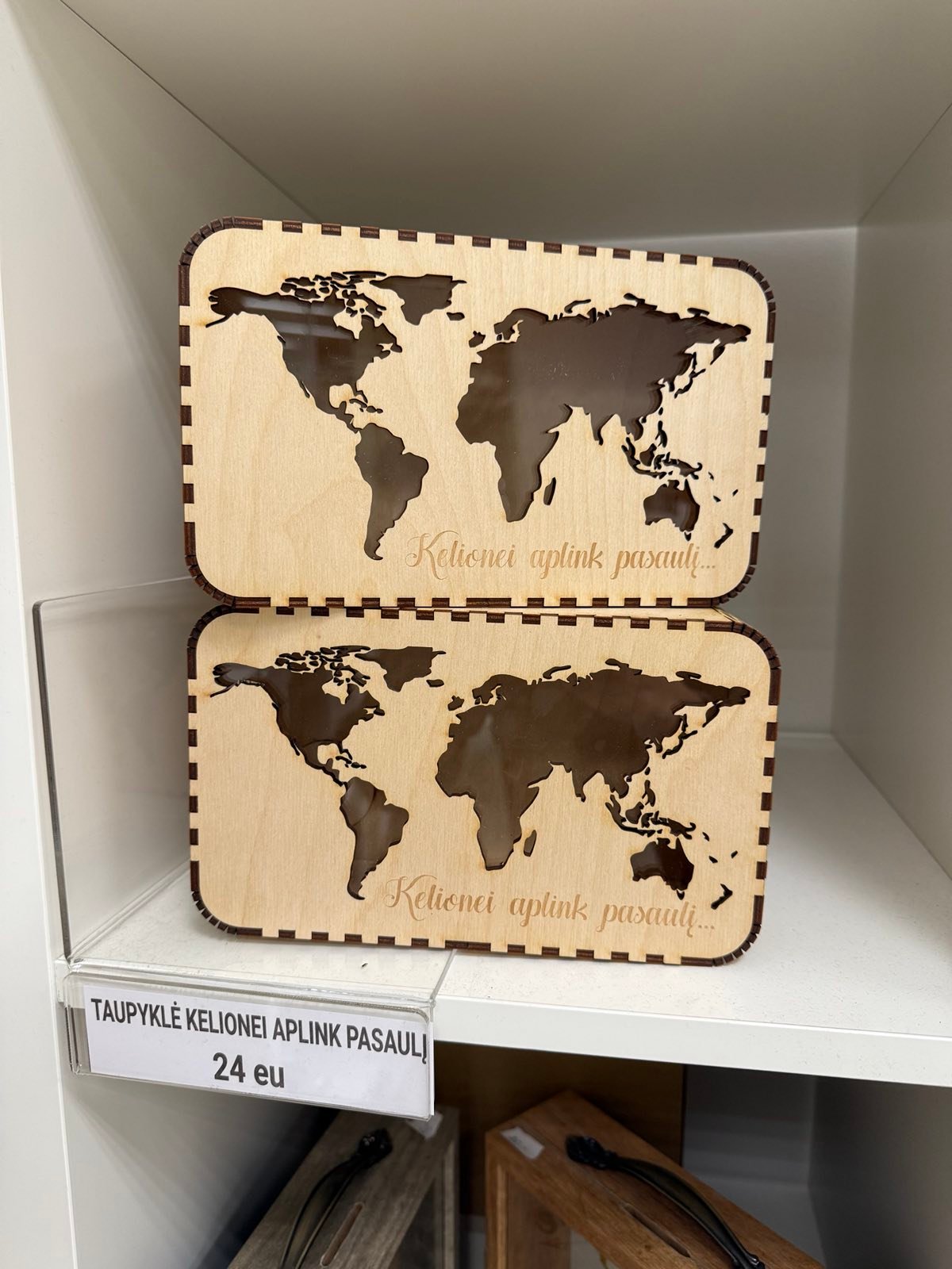 Nuotraukoje dvi natūralios medžio spalvos medinės taupyklės su graviruotu užrašu "Kelionei aplink pasaulį". Taupykle su išpjautu pasaulio kontūro langeliu, kad matytųsi taupymo kelionei progresas.