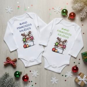 Du baltos spalvos kūdikių bodžiukai su ilgomis rankovėmis, papuošti kalėdine elniuko iliustracija ir užrašu "Mano pirmosios kalėdos", padėti ant šviesaus medinio paviršiaus, apsupti kalėdinių dekoracijų – žaisliukų, sniego snaigių ir eglių šakelių.