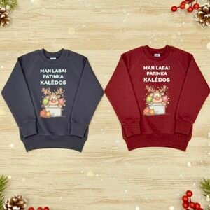 Du džemperiai vaikams su spalvota spauda. Džemperiai ilgomis rankovėmis, vienas tamsiai mėlynos (navy) spalvos, o kitas bordo, ilgomis rankovėmis, papuošti kalėdine elniuko iliustracija ir užrašu "Man labai patinka kalėdos", padėti ant šviesaus medinio paviršiaus, apsupti kalėdinių dekoracijų, sniego snaigių ir eglių šakelių.