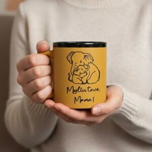 Nuotraukoje moteris laikanti geltoną puodelį stambiu planu. Tai geltonas graviruotas puodelis su užrašu „Myliu tave, Mama!“ ir piešiniu, kuriame pavaizduota mama dramblė apsikabinusi su mažyliu drambliuku. Piešinys ir užrašas graviruotas, o graviūros spalva - juoda. Puodelis 300 ml.